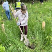 Kid digging a hole with a shovel at a planting event.