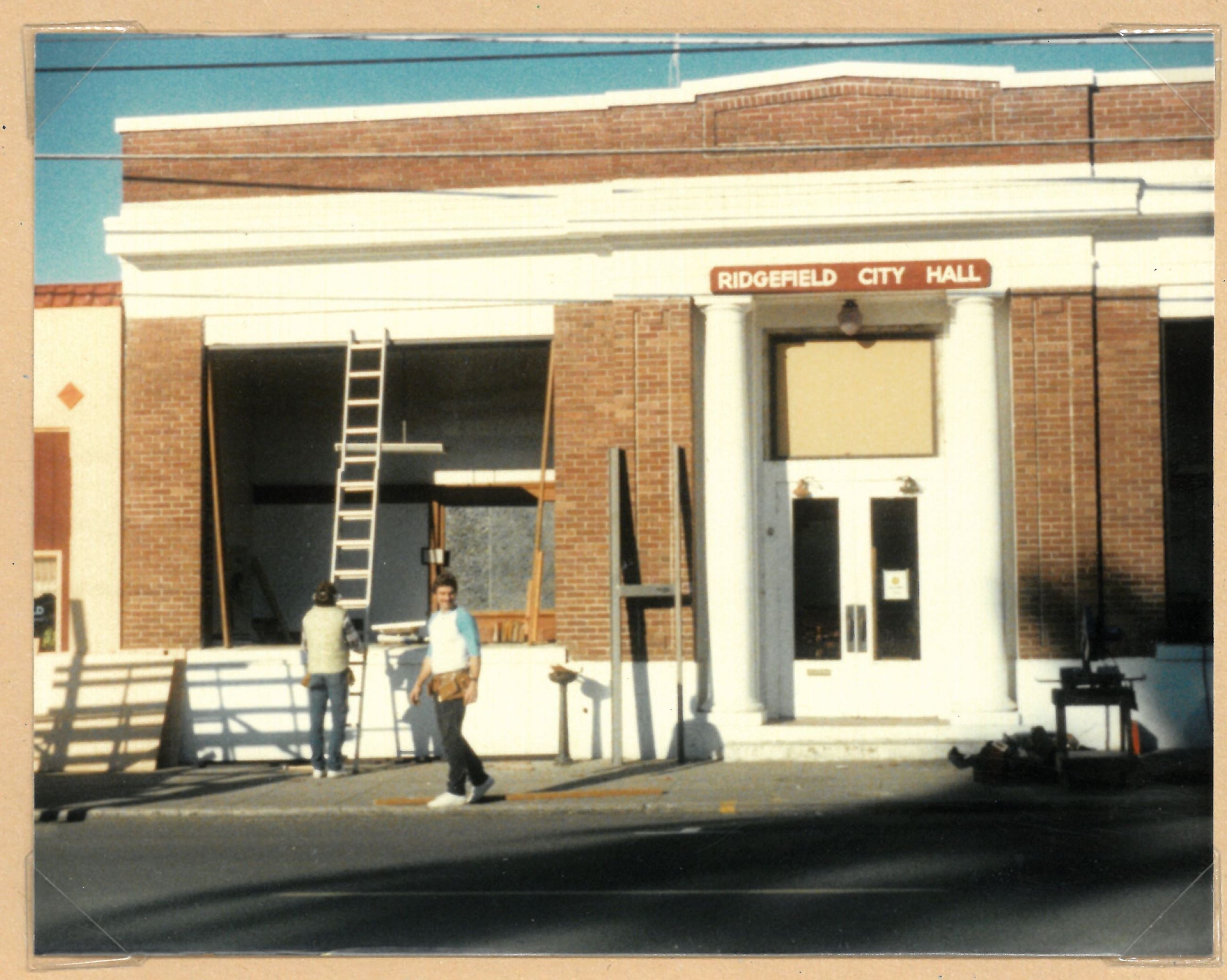 The front of the City Hall building with two men working to remove and replace the windows, 1985.
