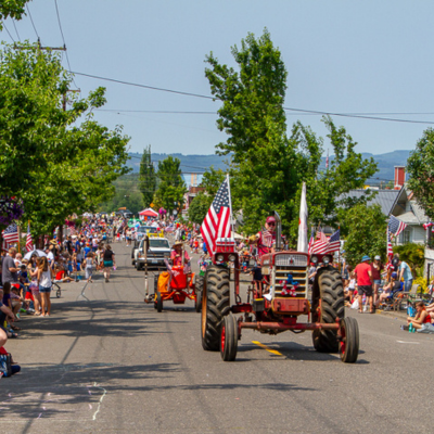 A tractor and other floats travel down the street for the 4th of July Parade.
