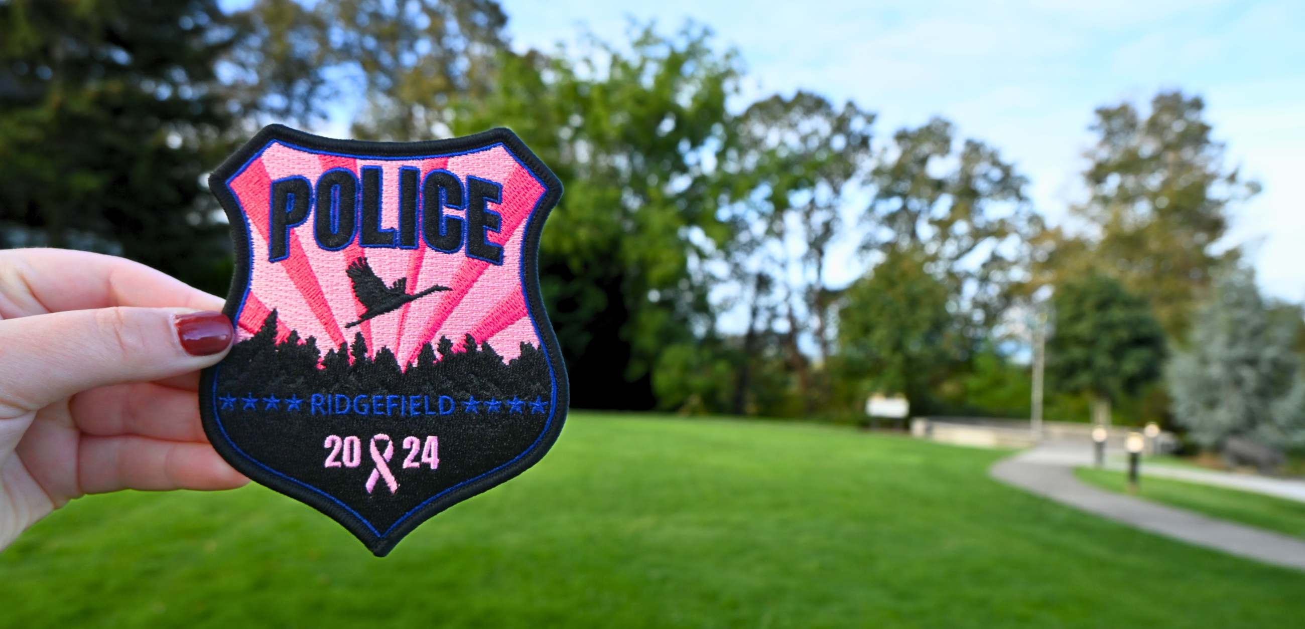 The 2024 Ridgefield Police Pink Patch in the foreground with greenery at Overlook Park in the back.